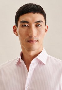 Camicia da uomo rosa chiaro con sottili righe bianche verticali, colletto button-down e texture liscia, indossata da una persona con capelli corti.
