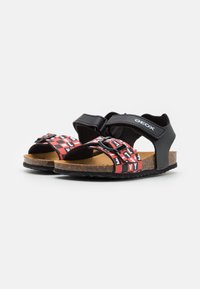 Sandalias negras con correas estampadas en rojo y blanco, cierre de velcro ajustable, plantilla de corcho y suela de goma texturizada. Logotipo de Geox visible.
