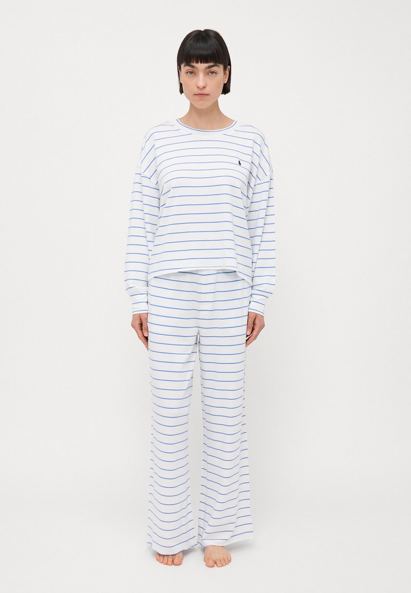 Witte pyjama-top met lange mouwen en blauwe strepen, gecombineerd met bijpassende wijde broek, gemaakt van zacht materiaal, met een klein logo op de borst.