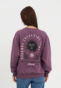 Paarse sweatshirt met een grafische print van een zon en tekst op de achterkant. Heeft een ronde hals, lange mouwen en geribde manchetten.