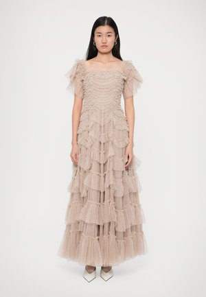 Tyllkjol i mjuk beige med rynkade lager, av-axeln puffärmar och en flödande silhuett, kompletterad med spetsiga vita klackar.