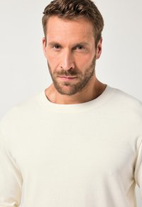 Kremfarvet langærmet skjorte lavet af blødt stof med rund halsudskæring og subtile syninger på kraven og ærmerne.