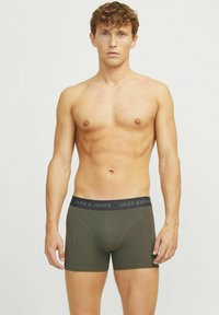 Olijfgroene boxershorts met een zwarte tailleband waarop de merknaam "JACK & JONES" staat. Gladde textuur en getailleerd ontwerp.