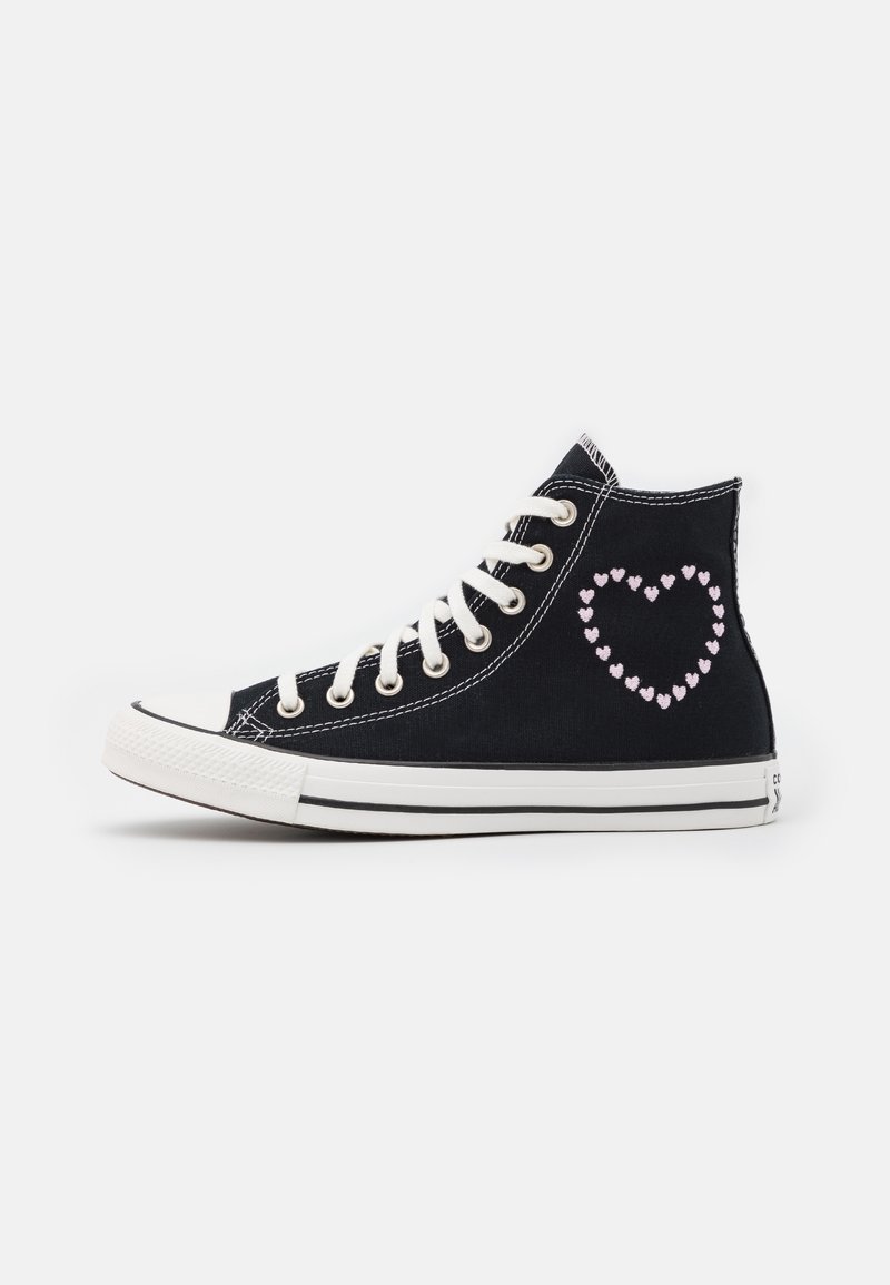 Basket montante noire avec lacets et semelle blancs, présentant une forme de cœur composée de petits cœurs roses sur le côté.