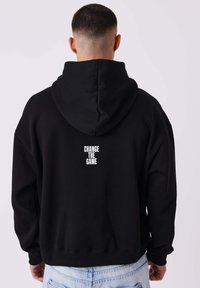Zwarte hoodie van katoen, met een grote capuchon, geribbelde manchetten en de tekst "CHANGE THE GAME" in het wit op de achterkant.