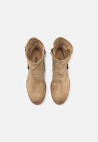 Botines de ante beige con una textura suave, punta redonda y una cremallera ajustable en el lateral, con una suela marrón clara.