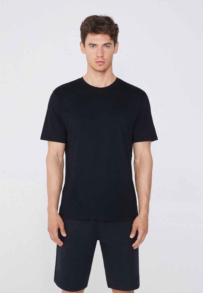 Camiseta de algodón negra de manga corta, con cuello redondo y un ajuste relajado, combinada con pantalones cortos oscuros a juego, textura suave y diseño minimalista.