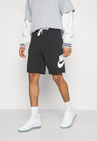 Nike mörkgrå shorts med vitt logo, elastisk midja med dragsko, matchat med en grå och vit lagertröja och vita sneakers.