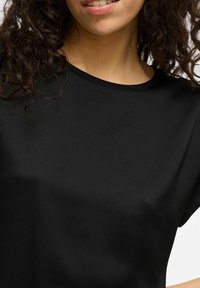 T-shirt noir à manches courtes en tissu lisse avec un col rond, présentant un design simple sans motifs ni embellissements.
