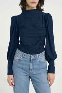Marineblå langermet bodysuit med puffede ermer og side-ruffling, kombinert med lyseblå høytlivd denimjeans. Jevn tekstur.
