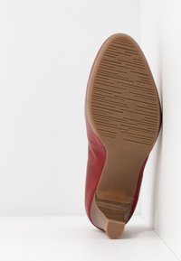 Chaussure à talon en cuir rouge positionnée debout avec semelle antidérapante visible et talon, taille 39, sur fond blanc.