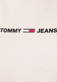 Camiseta de algodón blanca con un texto negro destacado que dice "TOMMY" y "JEANS", con un diseño de bandera de colores entre las palabras.