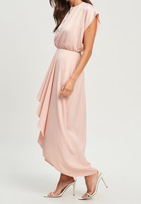 Pale pink satin dress with a flowing design, short sleeves, and a gathered waist. Features a draped skirt and metallic high heels.