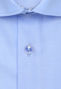 Chemise bleu clair avec un tissu lisse et texturé ; elle présente un bouton à motif floral et un col classique.