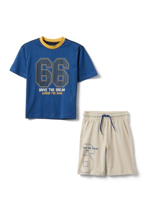 Camisa azul de manga corta con cuello amarillo y texto "66 Drive the Dream Across the Sand", pantalones cortos elásticos beige con cordón azul y número 6 impreso.