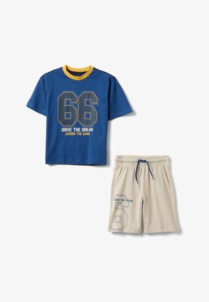 Camisa azul de manga corta con cuello amarillo y texto "66 Drive the Dream Across the Sand", pantalones cortos elásticos beige con cordón azul y número 6 impreso.