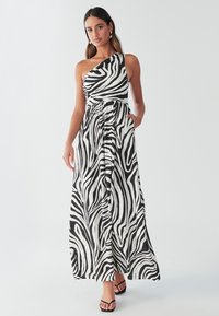 Maxikleid im Zebramuster mit einem einzelnen Schulterriemen, tailliertem Schnitt und Taschen. Hergestellt aus leichtem Stoff in Schwarz und Weiß.