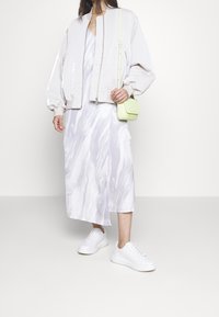 Světlounce šedá bomber bunda, středně dlouhé šaty s bílým mramorovým vzorem, bílé tenisky a malá, jasně zelená taška přes rameno. Jednoduchý a moderní design.