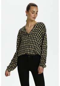 Langärmlige Bluse mit einem grünen, beigen und schwarzen Diamant-Muster. Glattes, leichtes Gewebe mit V-Ausschnitt und lockerer Passform.