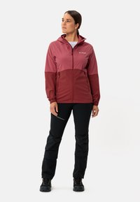 Maroon and pink two-toned hooded jacket with zip closure, paired with black pants featuring textured accents and sturdy footwear.