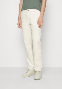 Pantalon en coton blanc avec un design à jambe droite. Comprend des poches avant et une fermeture à bouton. Associé à des baskets de couleur claire et une chemise verte.
