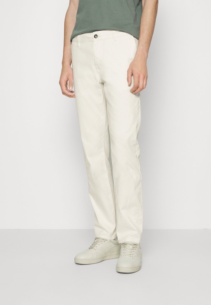 Pantalon en coton blanc avec un design à jambe droite. Comprend des poches avant et une fermeture à bouton. Associé à des baskets de couleur claire et une chemise verte.