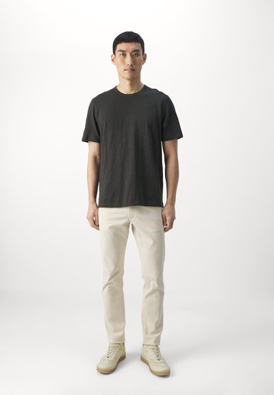 Black short-sleeve t-shirt, light beige slim-fit pants, and beige sneakers; model stands against a plain white background.