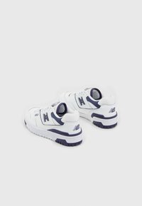 Vita idrottsskor i vitt med en strukturerad läderfinish, med marinblå detaljer, en tjock mellansula och varumärkesdetaljer på hälen.