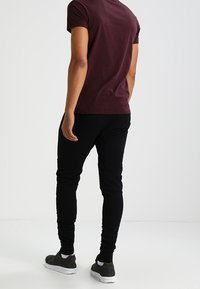 Bordová tričko s krátkým rukávem a černé slim-fit kalhoty, doplněné tmavými teniskami, zobrazené zezadu na neutrálním pozadí.
