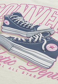 Baskets Converse navy avec des coutures et des lacets blancs, présentées contre un fond beige clair, arborant un texte rose et un logo.