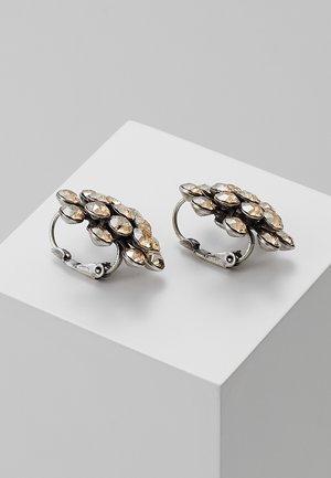 Zilveren clip-oorbellen met gegroepeerde, champagnekleurige edelstenen in een bladachtige compositie op een wit voetstuk.