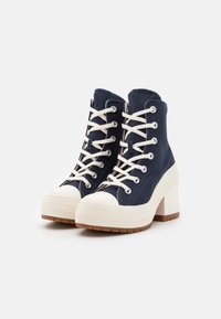 Sneakers alta navy con punta in gomma bianca, lacci crema e suola piatta beige testurizzata. Presentano occhielli in argento e dettagli cuciti.