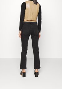 Tan faux läderkort vest med dragkedja baktill, kombinerat med åtsittande svarta jeans och svarta sandaler med klossklack. Slät textur.