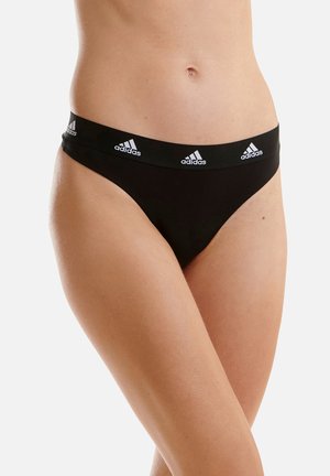 Schwarze Tanga-Unterwäsche mit einem weichen, elastischen Bund, der mit wiederholtem weißen "adidas"-Branding versehen ist. Glatte Textur und minimalistisches Design.
