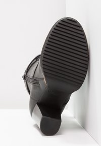 Botín de cuero negro a la altura del tobillo que presenta una suela de goma texturizada, tacón cuadrado y cremallera lateral. La suela cuenta con estrías horizontales para mayor agarre.