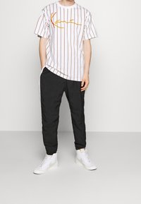 Camiseta blanca a rayas con gráfico en cursiva naranja y rojo, combinada con pantalones ajustados negros y zapatillas altas blancas.