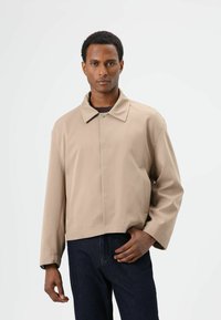 Beige cropped jack met een rechte snit, grote kraag en knoopsluiting. Gladde textuur, twee zijzakken en een eenvoudig ontwerp.