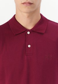 Bordeaux polo skjorte i bomuldsblanding med krave, to hvide knapper og præget "GAP" logo på venstre bryst.