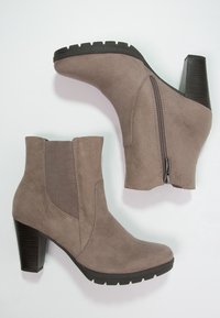 Taupe mockasiner med rund tå, sidodragkedja och klack i stapel. Texturerade elastiska paneler på sidorna ger designdetaljer.