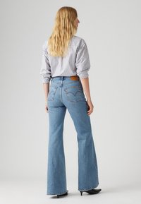 Jean flare bleu ciel avec une texture délavée et des coutures contrastantes. Associé à une chemise à rayures et des chaussures à talons noires.