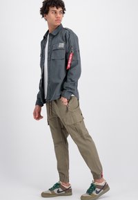 Gray button-up shirt with a patch and a zippered pocket, paired with light green cargo pants and patterned sneakers.