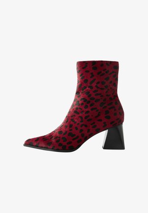 Bottines en daim rouge avec imprimé léopard noir, bout pointu et talon épais noir. Texture lisse avec un design ajusté.