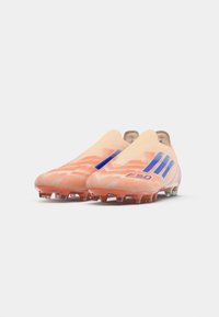 Un par de botas de fútbol en melocotón y azul con suelas con tacos, diseño sin cordones y la marca "F50" en un fondo blanco.
