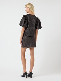 Juodos tekstūros trumpomis pūstomis rankovėmis viršus, derantis su mini sijonu. Dėvima su juodais aukštakulniais batais.