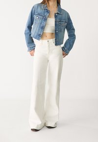 Denimjacka med ljusblå tvätt, två framfickor och knappstängning, tillsammans med högmidjade vida vita byxor.