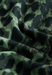 Close-up af mørkegrønt og sort camouflage-stof med bløde folder og en glat tekstur.