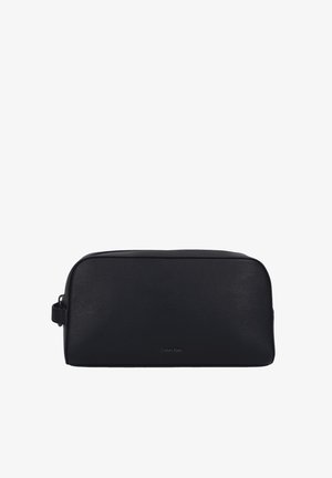 Trousse de toilette en cuir noir avec une forme rectangulaire, une surface texturée, une fermeture éclair sur le dessus et une poignée latérale. Marquée du logo "Calvin Klein".