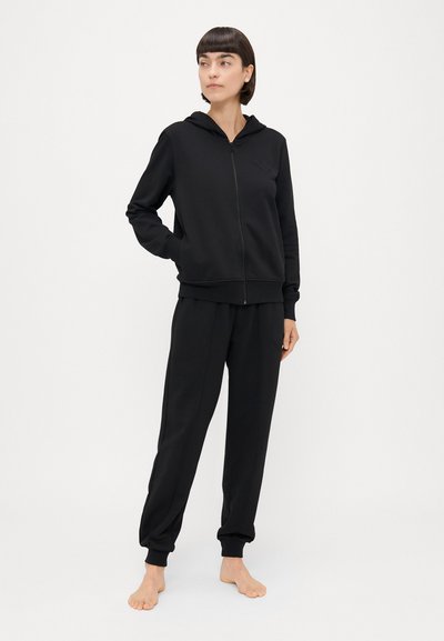 Črna zip-up kapuca z mehko teksturo in sprednjim žepom, v kompletu z ustreznimi tesnimi hlačnicami s elastičnimi manšetami in subtilnim logotipom.