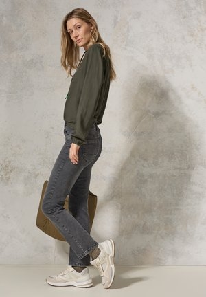 Olijfgroene lange mouwen top gecombineerd met donkergrijze jeans en witte sneakers. De outfit heeft een relaxte pasvorm en soepele texturen.
