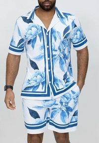 Ensemble composé d'une chemise à manches courtes et d'un short, de couleur blanche avec des imprimés floraux bleus, des rayures horizontales et une fermeture à boutons. Tissu léger.